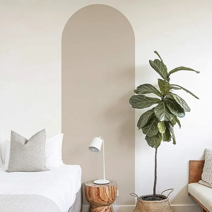 Vinilo de pared autoadhesivo Arco Topo - 65 x 200 cm, Topo, Plástico - Una higuera de hoja de violín en una cesta tejida se sienta junto a una mesita de noche con una lámpara moderna, creando un ambiente acogedor y natural.