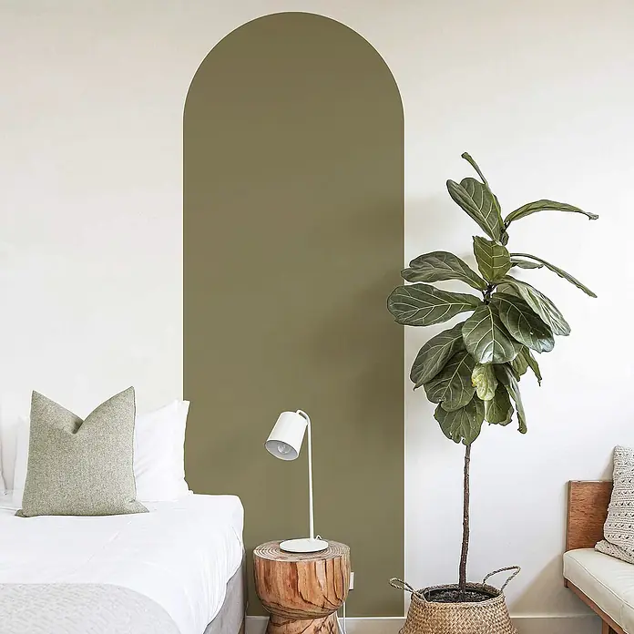 Vinilo de pared autoadhesivo Arco Verde Oliva - 65 x 200 cm, Verde, Plástico - Interior de habitación con arco pintado de verde, cama, lámpara, taburete de madera y planta de interior en cesta.
