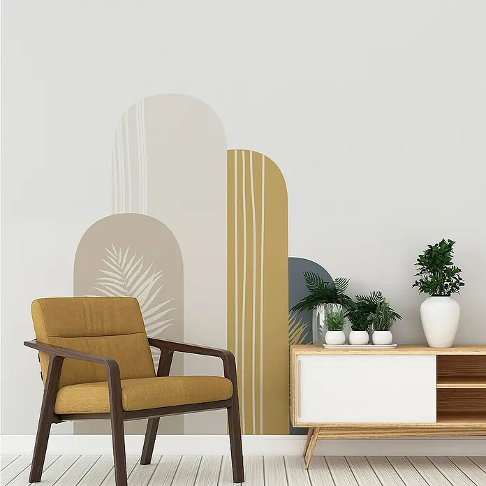 Vinilo de pared autoadhesivo Arco Eros - 132 x 170 cm, Multicolor, Plástico - Interior con un sillón amarillo y una cómoda con plantas, frente a una pared con formas abstractas.