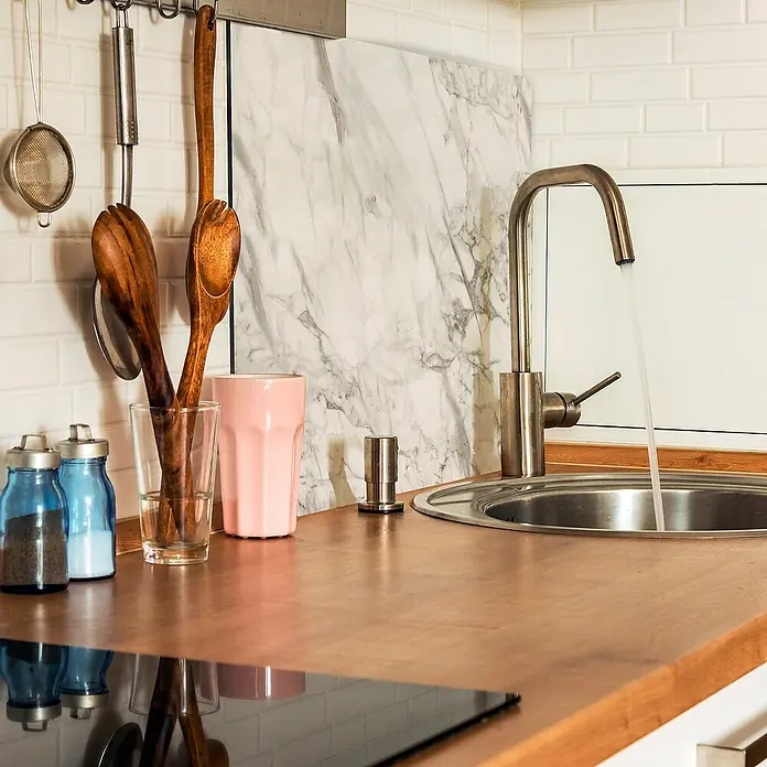 Panel de pared salpicadero de cocina Marble - L x An: 60 x 60 cm, Café - Primer plano de un fregadero de cocina con grifo, encimera de madera y varios utensilios de cocina al fondo.