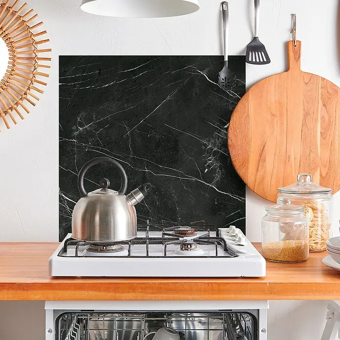 Panel de pared salpicadero de cocina Marquina - L x An: 60 x 60 cm - Escena de cocina con protector contra salpicaduras de mármol negro detrás de una cocina de gas blanca, con un hervidor plateado encima. ¡Práctico y elegante!