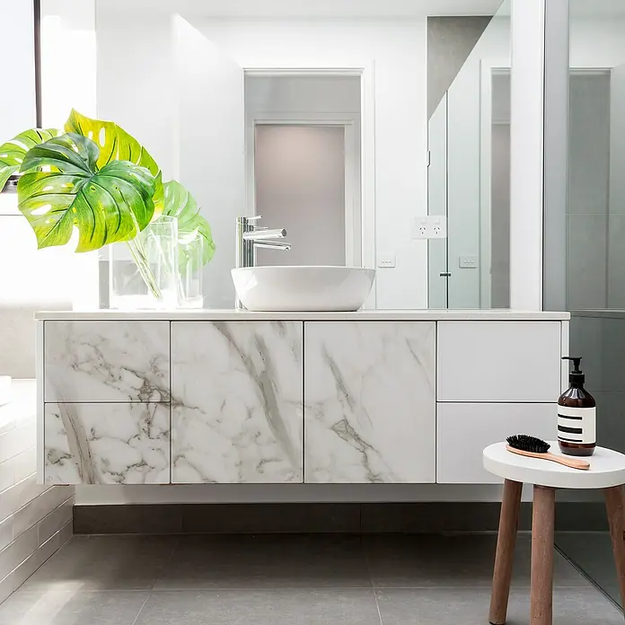 Vinilo de pared autoadhesivo Brown jasper - Blanco/Marrón, 200 x 100 cm - Un baño moderno con un elegante tocador de mármol, un lavabo sobre encimera blanco y plantas verdes para la decoración.