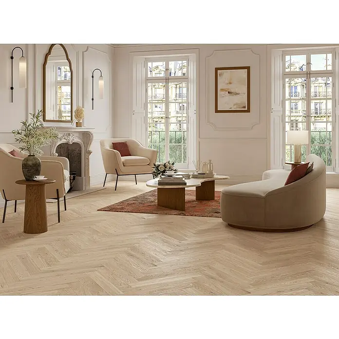 Parador Parkettmuster Trendtime 3 Living Plus Eiche Bardolino weiß - 200 x 95 x 13 mm, Fischgrät - Elegantes Wohnzimmer mit hellen Holzböden, beigen Sesseln und einem geschwungenen Sofa. Der Marmortisch und der Kamin verleihen dem Raum eine luxuriöse Note.
