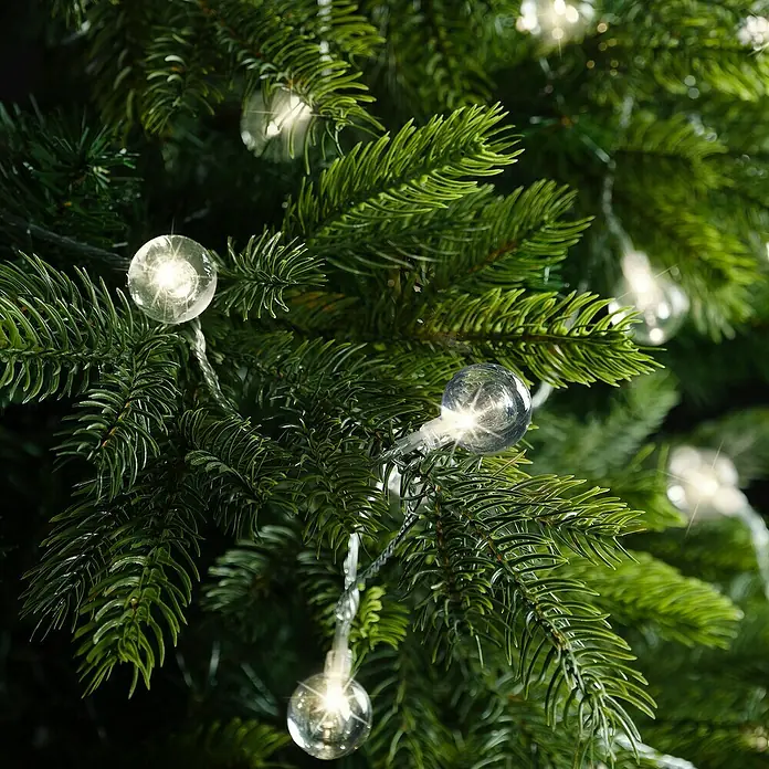 Guirnalda luminosa LED Cherry XL - Para interior, 9 cm, Blanco cálido, 60 ud. - Primer plano de una serie de luces con bombillas esféricas, fijadas a un árbol de Navidad verde, creando un ambiente festivo.