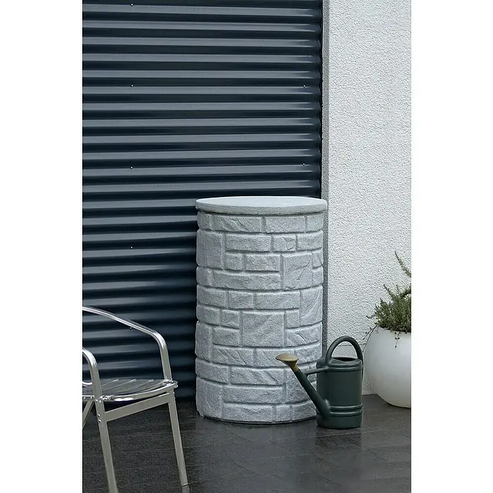 Arves Regenspeicher Arcado - 230 l, Granitfarben - Nahaufnahme eines Regentonne mit Steinmuster, neben einer Gießkanne und einem Stuhl.
