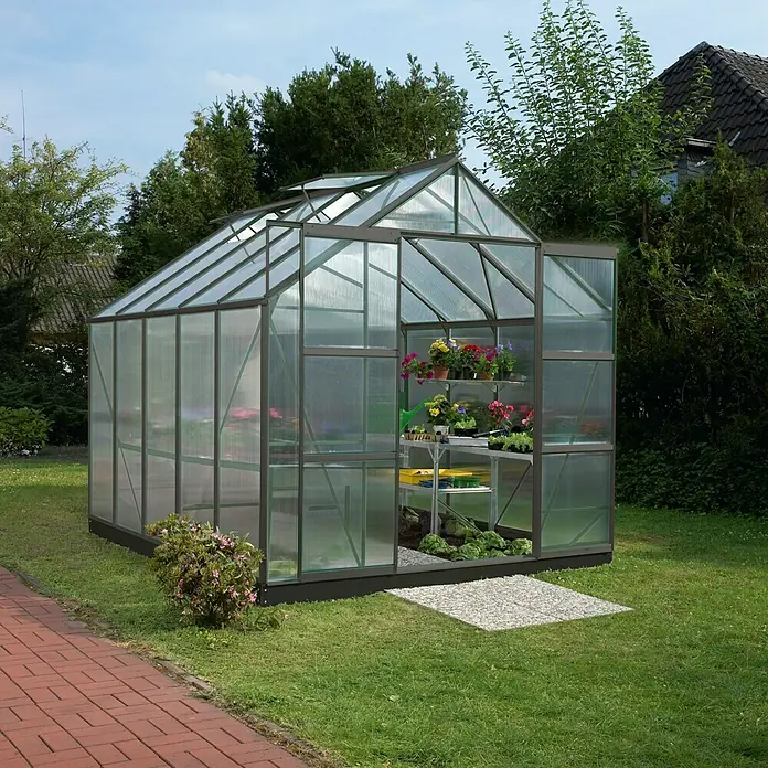 Vitavia Gewächshaus Mars 8300 Plus - Außenmaß inkl. Dachüberstand (B x T): 257 x 321 cm, 4 mm, Schwarz - Ein Gewächshaus mit Regalen voller Blumen und Pflanzen. Es steht in einem grünen Garten mit Bäumen und einem Haus im Hintergrund.