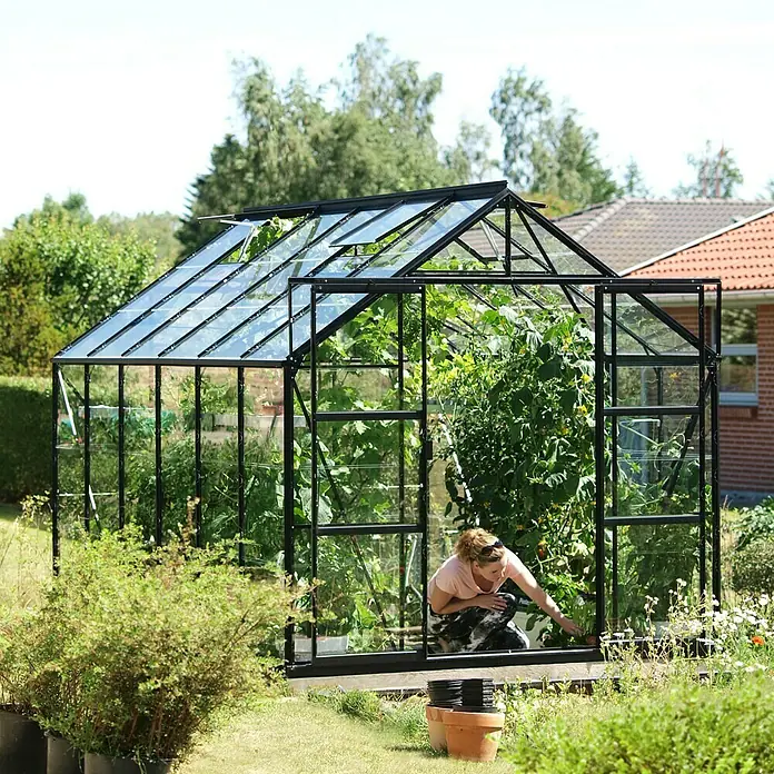 Vitavia Gewächshaus Uranus 9900 - Außenmaß inkl. Dachüberstand (B x T): 257 x 383 cm, 3 mm, Schwarz - Ein geräumiges Gewächshaus mit Pflanzen und einer Gärtnerin. Das Gewächshaus bietet ausreichend Platz für den Anbau verschiedener Pflanzen.