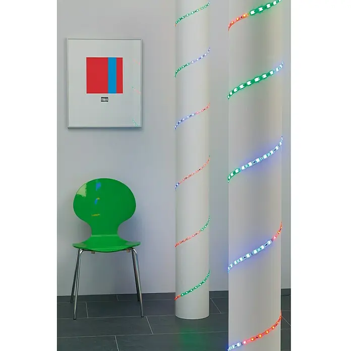 Prisma Leuchten LED-Band Flexband - Länge: 5 m, Mehrfarbig - LED-Lichterkette schlängelt sich um eine weiße Säule, daneben ein grüner Stuhl und ein gerahmtes Bild.
