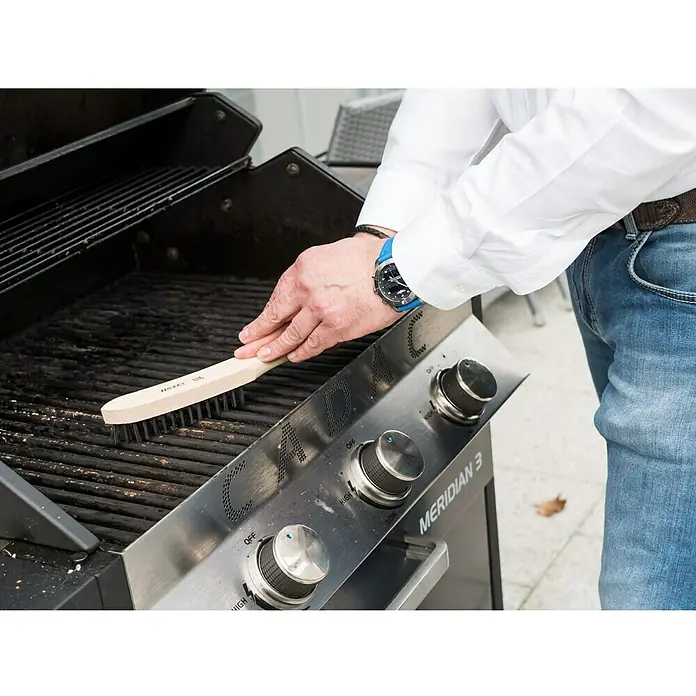 Hazet Drahtbürste 2130 - Anzahl Reihen: 4 Stk. - Ein Mann reinigt einen Grill mit einer Hazet Grillbürste, um ihn für das nächste Grillen vorzubereiten. Die Bürste entfernt Rückstände effektiv.