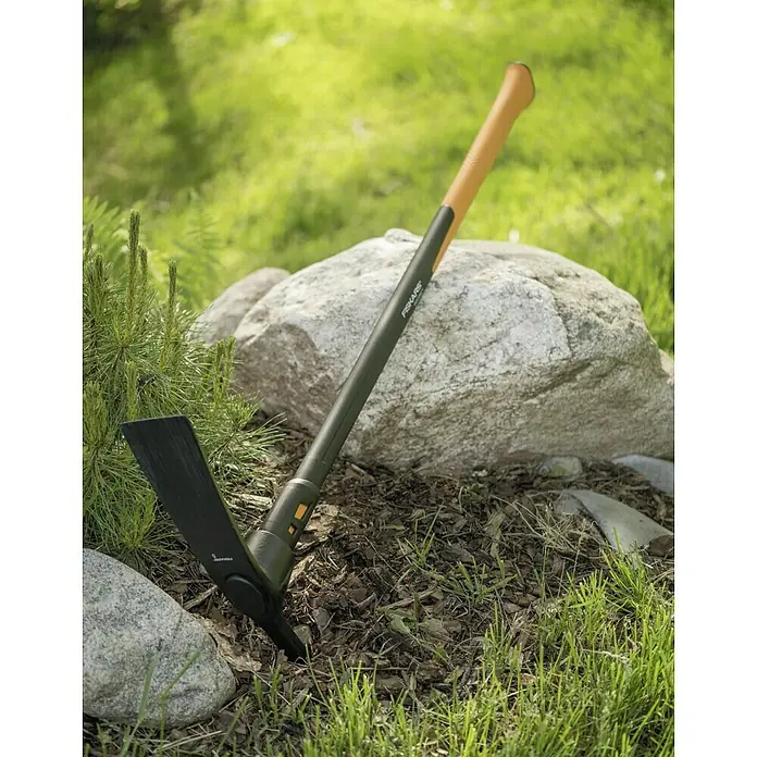 Fiskars Kreuzhacke L - Gewicht Kopf: 2.270 g - Nahaufnahme einer Fiskars Hacke mit orangefarbenem Griff vor einem Felsen.