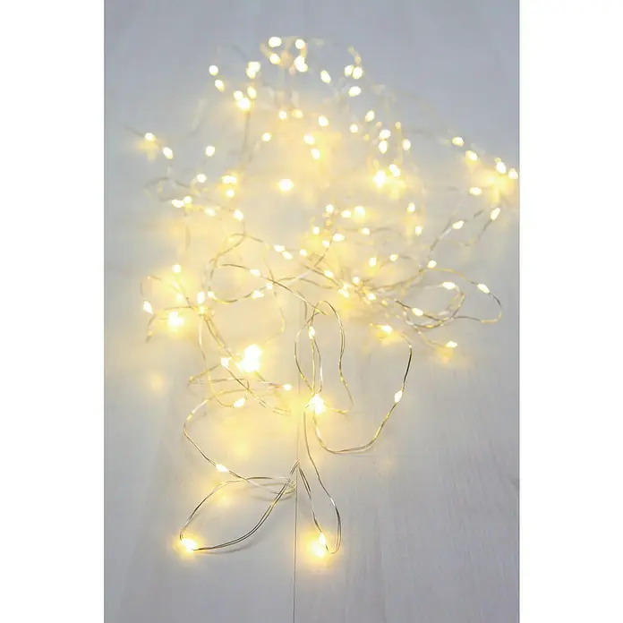 Globo Guirnalda luminosa LED Venuto - Para interior, Longitud del cable: 9,9 m, Transparente - Primer plano de una cadena de luces con luz blanca cálida sobre una superficie de madera clara. Las luces delicadas crean un ambiente festivo.