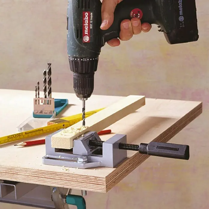 Wolfcraft Spannbacken - Spannweite: 65 mm - Eine Metabo Bohrmaschine bohrt ein Loch in ein Werkstück, das in einem Schraubstock auf einer Werkbank befestigt ist.