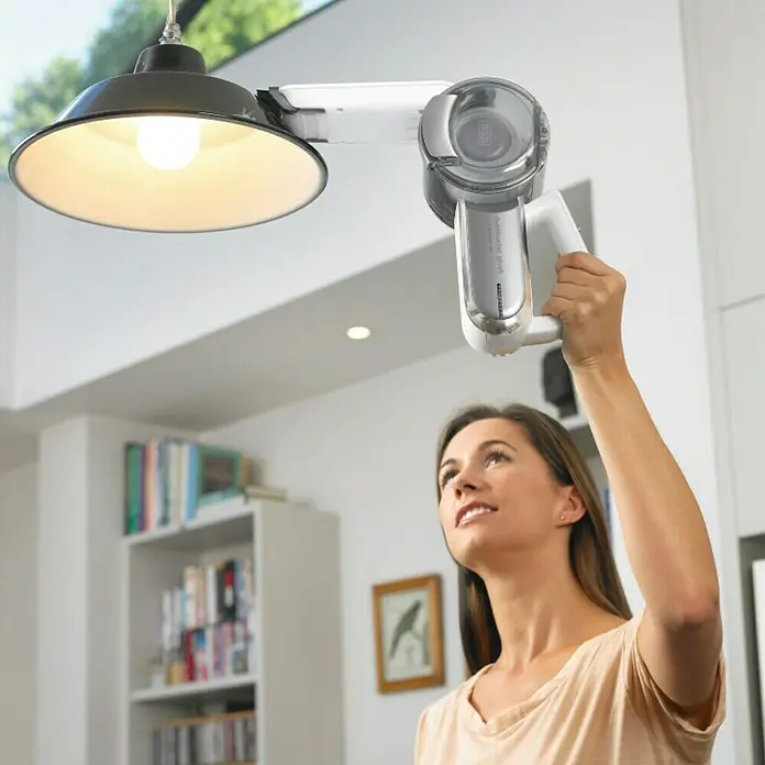 Black+Decker Aspirador de mano de batería PV1820L-AARU - 18 V, 1 batería, Volumen de recipiente: 440 ml - Mujer usa una aspiradora de mano inalámbrica Black+Decker para limpiar una lámpara. Práctico para lugares de difícil acceso.