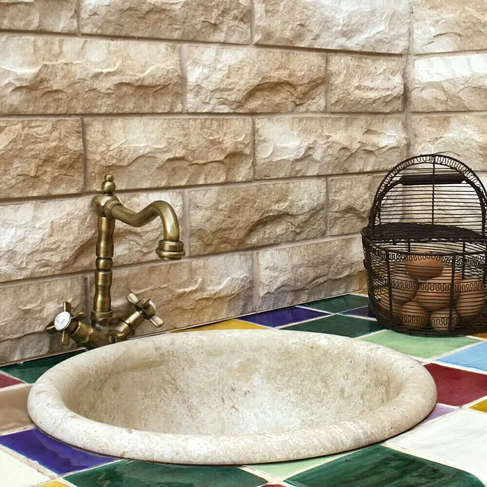 Revestimiento de piedra Cantabria - Pardo, Cantidad total: 4 pzs. - Un lavabo de piedra con accesorios de latón y una canasta de huevos de alambre, sobre un fondo de pared con diseño de piedra. El lavabo es el producto principal.