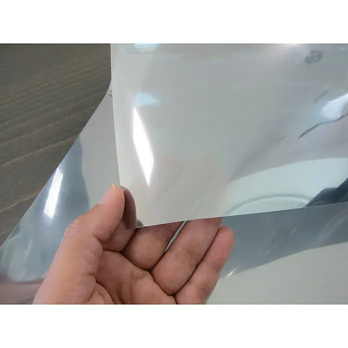 Lámina para ventana estático Efecto Espejo - 75 x 150 cm, Efecto espejo, Plateado - Primer plano de una mano sosteniendo una lámina de film transparente y brillante. Ideal para protección o manualidades, mostrando su flexibilidad.