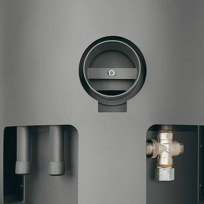 Justus Kaminofen Faro Aqua 2.0 - 8,5 kW, Raumheizvermögen: 200 m³, Material Verkleidung: Speckstein, Schwarz/Speckstein - Nahaufnahme eines Ofens mit Lüftungsöffnung, Rohren und einem Ventil. Das Design ist schlicht und industriell.