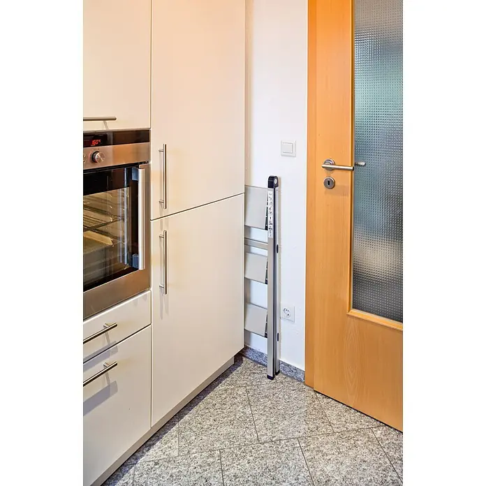 Stabilomat Basicline Klapptritt Slim - Anzahl Tritte: 3 Stk., Arbeitshöhe: 2,75 m, Belastbarkeit: 150 kg, Aluminium - Eine platzsparende, zusammenklappbare Tritthockerleiter aus Metall steht in einer Ecke neben einem Küchenschrank und einer Tür.