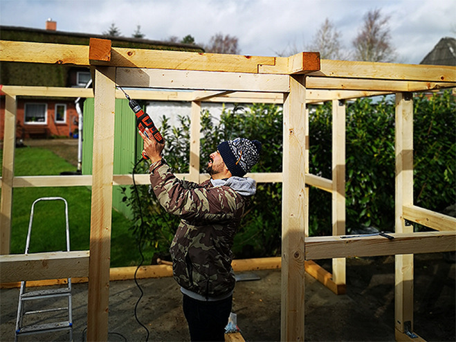 Mann mit Schlagbohrer beim Holzhütte selber bauen