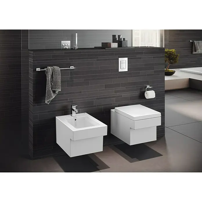 Grohe Essentials Cube Badetuchhalter - Breite: 55,8 cm, Chrom, Glänzend - Dieses Bild zeigt eine moderne Badezimmerinstallation mit einem wandhängenden Bidet und einer Toilette vor einer dunklen Wand.