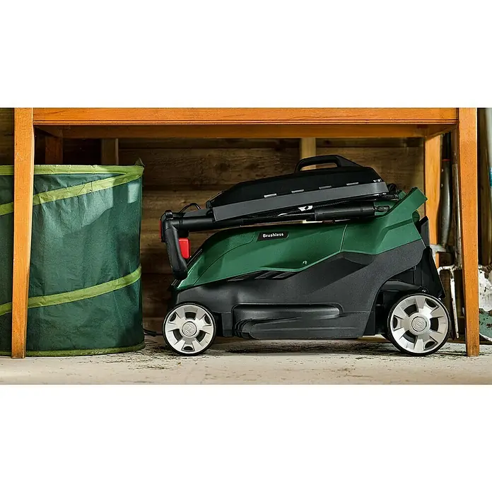 Bosch Power for All 36V Akku-Rasenmäher AdvancedRotak 36V-44-750 - 36 V, 1 Akku, 6 Ah, Schnittbreite: 44 cm - Zusammengeklappter Rasenmäher der Marke Bosch mit dem Schriftzug "Brushless" in einer Garage. Daneben steht ein Laubsack.