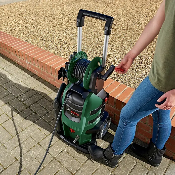 Bosch Hochdruckreiniger AdvancedAquatak 150 - 2.200 W - Eine Person bedient einen grünen Bosch Hochdruckreiniger im Freien mit Schlauchtrommel und Teleskopgriff.