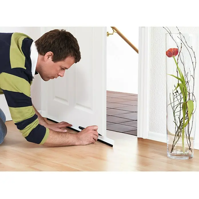 Tesa INSULATION Burlete para puerta Standard - 1 m x 12 mm, Puertas, Marrón - Un hombre coloca un burlete en la puerta para evitar corrientes de aire. Aislamiento eficaz para un hogar acogedor.