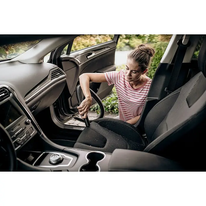 Kärcher Aspirador en seco y húmedo eléctrico WD 2 Plus - 1.000 W, Volumen de recipiente: 12 l, Con bolsa - Una mujer limpiando el interior de un coche con una aspiradora, centrándose en la aspiradora y el interior limpio.