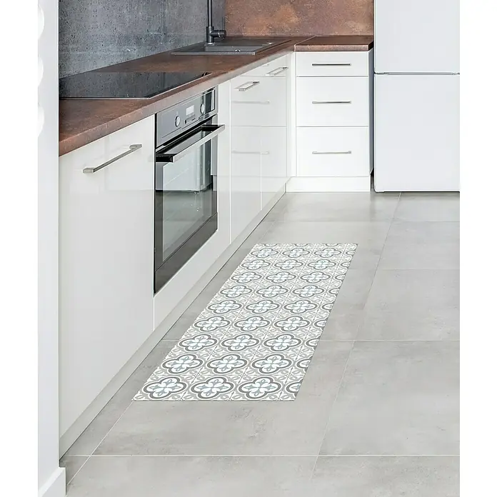 Alfombra de vinilo Croma Hidra topo - 140 x 50 cm - Un camino de cocina decorativo con un patrón de baldosas florales sobre un suelo de baldosas grises en una cocina moderna.
