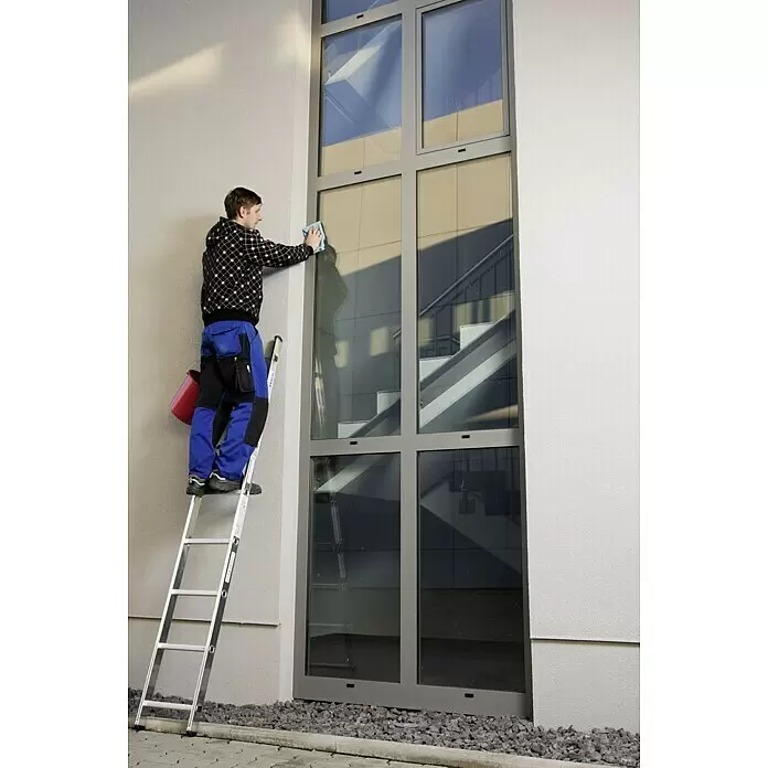 Krause Corda Escalera de apoyo - Número de peldaños: 8 ud., Altura de trabajo: 3,2 m, Carga soportada: 150 kg, Aluminio - Hombre en una escalera limpiando una gran ventana de múltiples paneles de un edificio moderno con un paño azul.