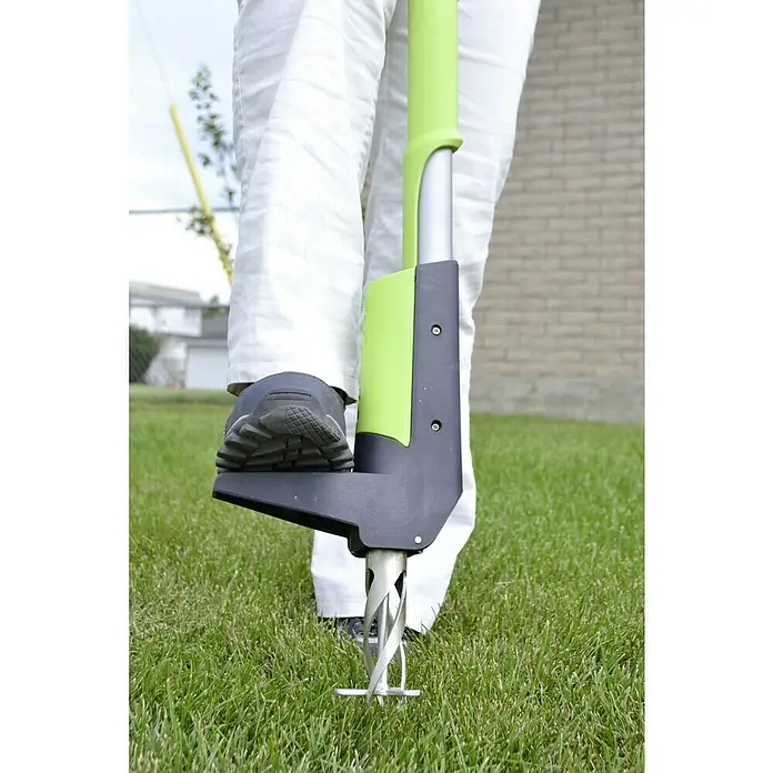 Freund Victoria Unkrautstecher - Mit Fußhebel, Länge: 102 cm - Nahaufnahme eines grünen Unkrautstechers mit Fußpedal, der in einen Rasen gesteckt wird.