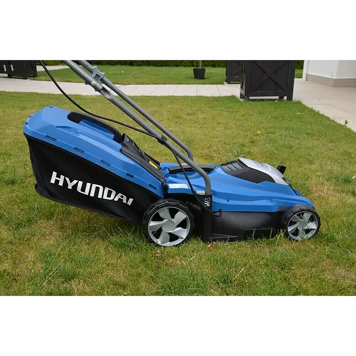 Hyundai Elektro-Rasenmäher LM3301E - 1.300 W, Schnittbreite: 33 cm - Ein blauer Hyundai Rasenmäher mit Fangkorb steht auf einem Rasen. Das Gerät ist mit grauem Griff ausgestattet.