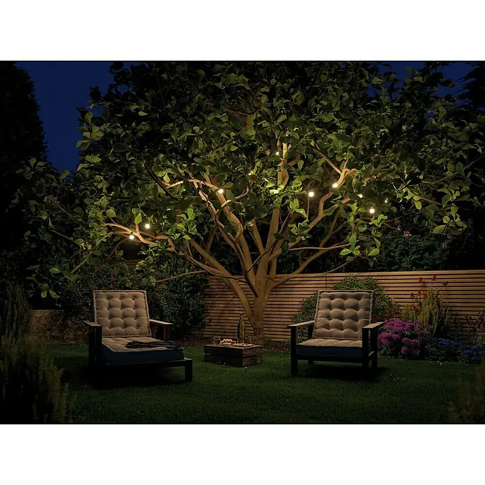 Paulmann Plug & Shine LED-Lichterkette - Außen, Lichtfarbe: Warmweiß, Anzahl Leuchtmittel: 7 Stk. - Gartenmöbel mit Sesseln, kleinem Tisch und Lichterketten im Baum. Das Ambiente lädt zum Verweilen im Freien ein und bietet eine gemütliche Atmosphäre.