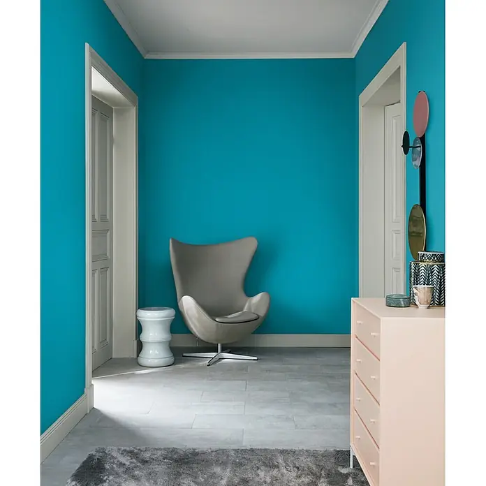 SCHÖNER WOHNEN-Farbe Wandfarbe Trendfarbe - Lagune, Matt, 2,5 l - Einladender Raum mit türkisblauen Wänden, einem grauen Sessel und einer rosa Kommode, der eine moderne und stilvolle Atmosphäre schafft.