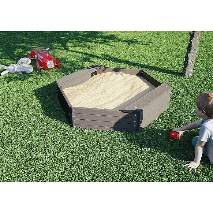 Kiehnholz SandkastenDurchmesser: 109 cm, BPC - Ein sechseckiger Sandkasten aus Holz mit Sand gefüllt, umgeben von Spielzeug und Gras.