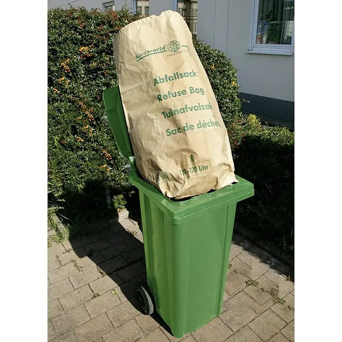 Floraworld Classic Papiersack - 110 l - Ein voller, hellgrüner Abfallbehälter mit einem großen, beigefarbenen "Floraworld"-Abfallsack darauf, vor einem grünen Busch.