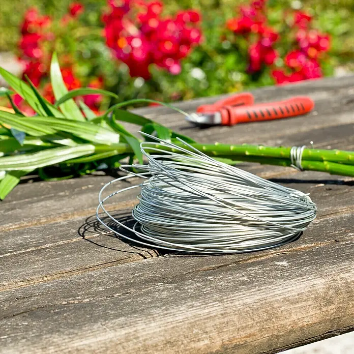 Gardol Gartendraht - 1,8 mm x 20 m, Verzinkt - Nahaufnahme einer Rolle Blumendraht auf einer Holzoberfläche mit Pflanzen und einer Gartenschere im Hintergrund.