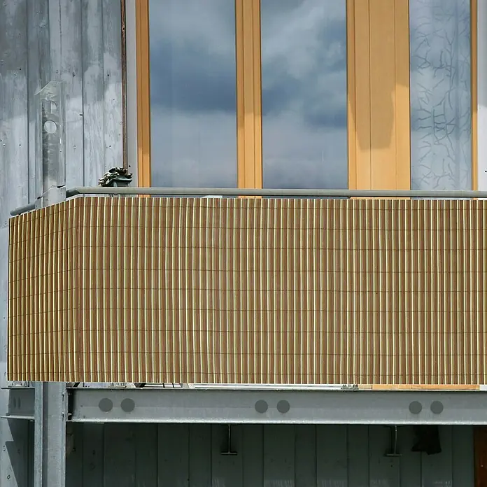 Gardol Balkonsichtschutz Eco - Bunt, Bambus Optik, 300 x 90 cm - Nahaufnahme eines Balkons mit Bambusverkleidung und einer modernen, grauen Fassade. Fenster reflektieren den Himmel.
