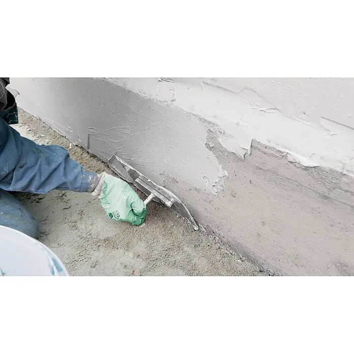Ultrament Reaktivabdichtung - 20 kg, 2-komponentig - Ein Arbeiter glättet mit einer Glättkelle eine Wand, um eine ebene Oberfläche für weitere Bauarbeiten zu schaffen.