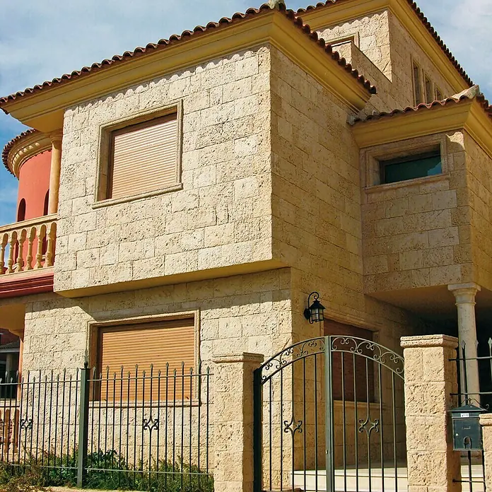 Revestimiento de piedra Coral Piedra - Coral - Primer plano de una casa con una puerta de hierro forjado y persianas marrones para un aspecto cálido y acogedor.