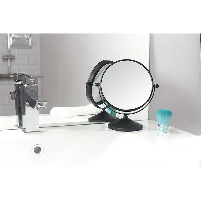 Deblanch Espejo cosmético - 15 x 15 cm, Redonda, Negro, Aumento 1: 700 % - Primer plano de un espejo cosmético sobre una mesa de baño con un cepillo. Diseño elegante con funcionalidad práctica para la rutina de belleza diaria.