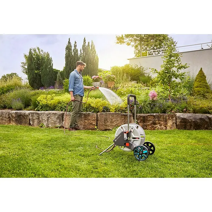 Gardena Kit carro portamangueras AquaRoll M - Metal, Longitud del tubo: 30 m - Un hombre riega su jardín con una caja de manguera Gardena sobre ruedas, que se puede mover y guardar fácilmente.