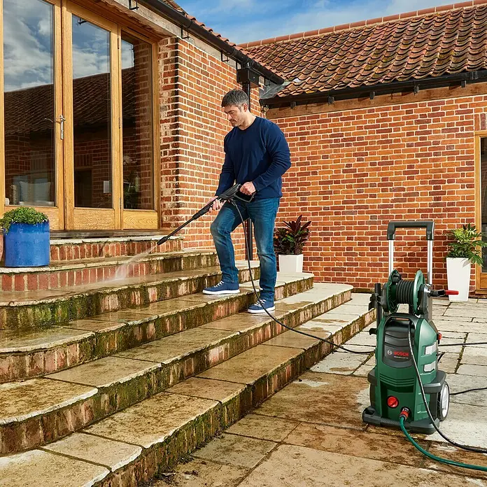 Bosch Hochdruckreiniger AdvancedAquatak 160 - 2.600 W, Max. Druck: 160 bar, Fördermenge: 570 l/h - Ein Mann reinigt mit einem Bosch Hochdruckreiniger eine Treppe vor einem Backsteingebäude. Ideal für Haus und Garten.