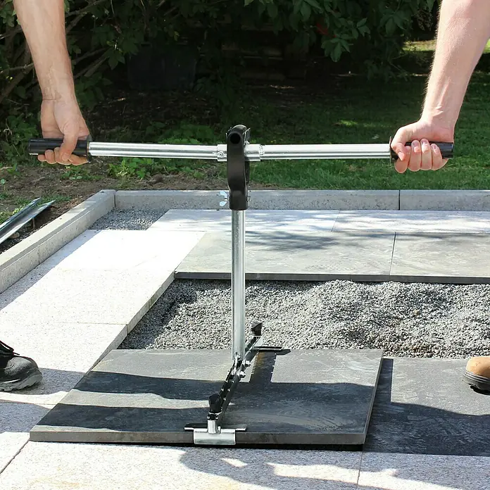 Langfit Plattenheber-Tragarm MS-PH2TA - Passend für: Langfit Platten- und Fliesenheber, Geeignet für: 2 Personen, Tragkraft: 60 kg - Nahaufnahme eines manuellen Pflastersteinspalters, der von zwei Personen bedient wird, um einen Stein auf einer gepflasterten Fläche zu spalten.
