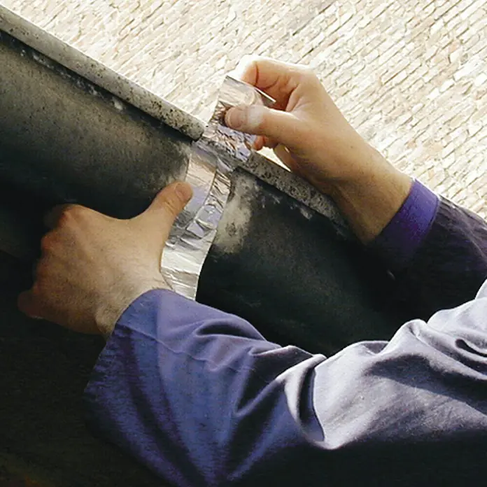 Tesa Cinta de aluminio - Plata, 10 m x 50 mm - Una persona que aplica una cinta adhesiva impermeable y duradera para la reparación de tuberías, asegurando durabilidad y sellado hermético.