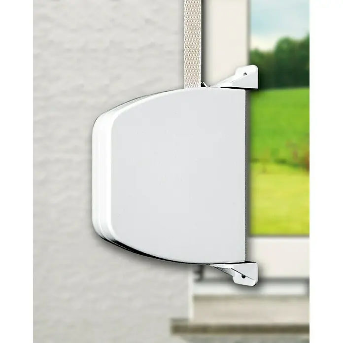 Schellenberg Recogedor de cinta de persiana Mini - Montaje en la pared, Anchura de la correa: 14 mm, Blanco - Primer plano de un mecanismo de persiana enrollable blanca con una cinta y una ventana al fondo.