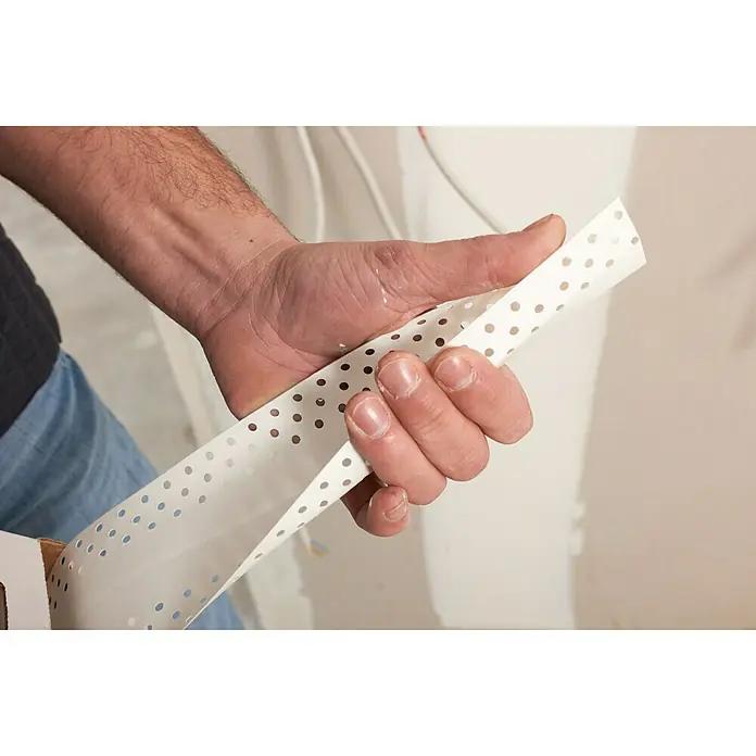 Rigips Kantenschutz für Trockenbau Aqua Bead - 25 m, Kunststoff, Flexibel - Eine Hand hält eine perforierte Gipskartonband, ein wichtiges Material für Trockenbauarbeiten, um glatte Übergänge zu gewährleisten.