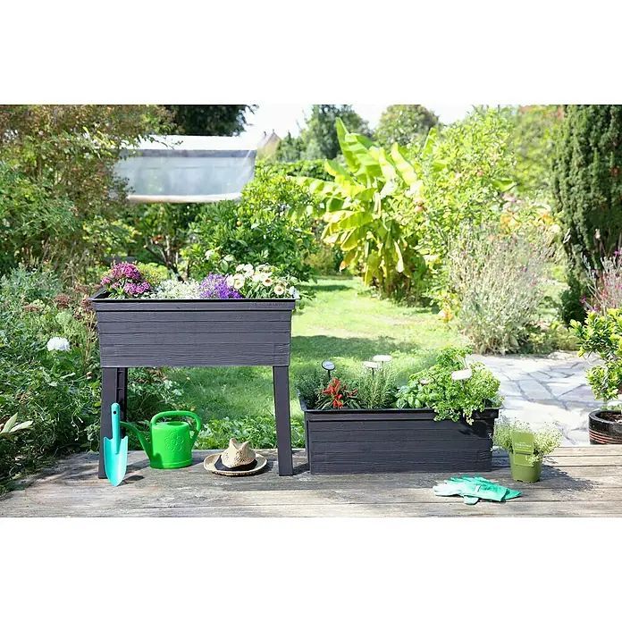 Garantia Urban Hochbeet - 75 x 37 x 65 cm, Kunststoff, Anthrazit - Ein erhöhter, dunkelgrauer Pflanzkasten aus Holzimitat mit bunten Blumen und einem flachen Pflanzkasten, umgeben von Gartengeräten.
