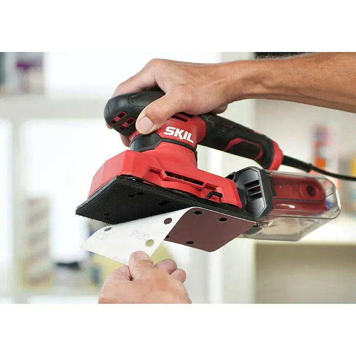 Skil Elektro-Schwingschleifer 7362 AA - 280 W - Nahaufnahme eines SKIL-Elektroschleifers, bei dem Schleifpapier angebracht wird. Ideal für DIY-Projekte und Heimwerkerarbeiten.