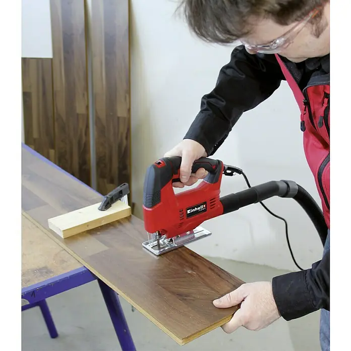 Einhell Elektro-Stichsäge TC-JS 60/1 - 1.000 /min - 3.000 /min, 60 mm - Ein Mann arbeitet mit einer roten Einhell Stichsäge, um ein Stück Holz zu schneiden. Die Säge ist mit einem Staubsauger verbunden.