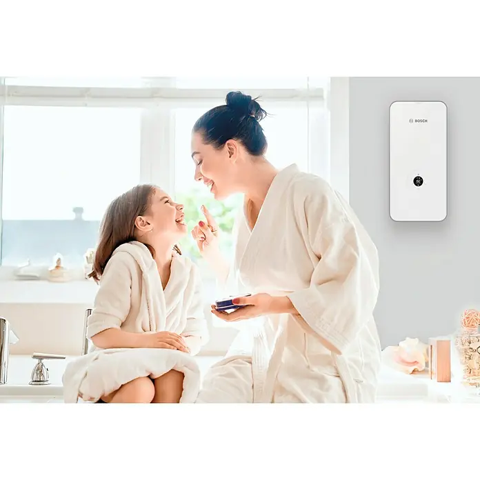 Bosch Durchlauferhitzer Tronic Excellence AquaStop - 15/18/21 kW, Elektronisch - Ein modernes Bosch-Warmwassergerät hängt an der Wand, während Mutter und Tochter sich im Bad verwöhnen. Praktisch und komfortabel.